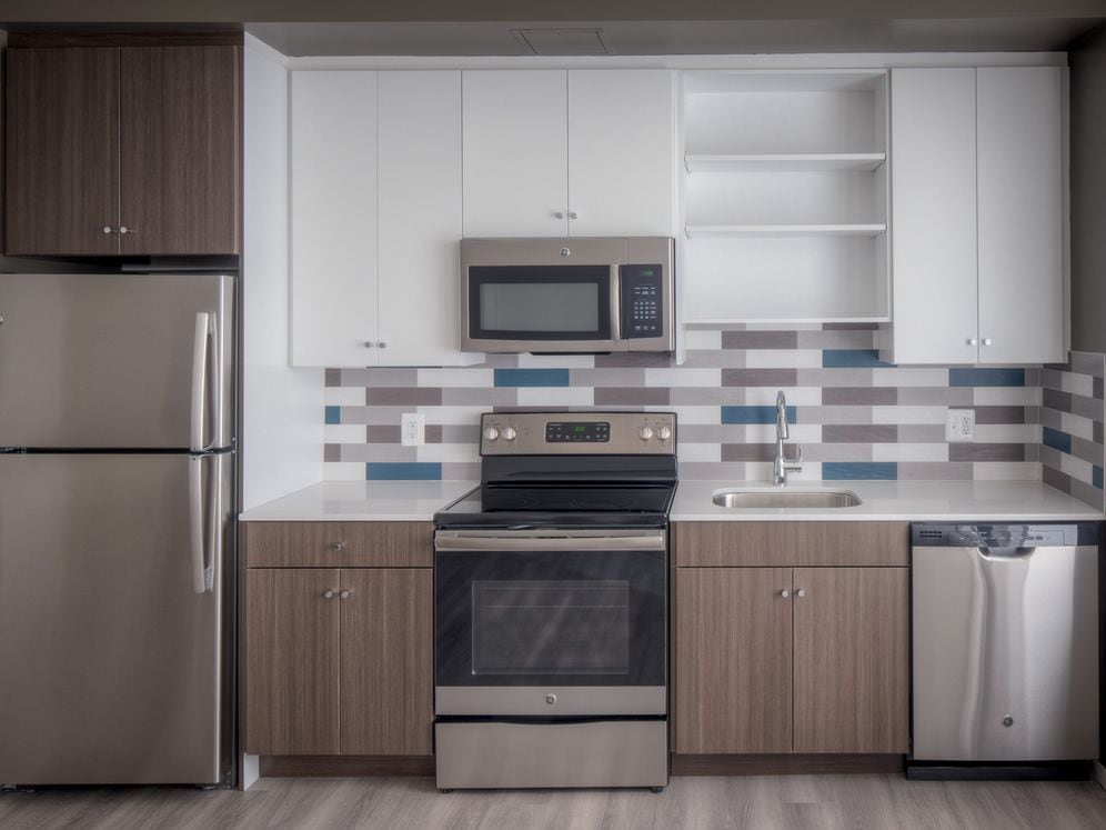 Kitchen with two tone cabinetry, quartz countertop, stainless steel appliances, tile backplash and hard surface flooring