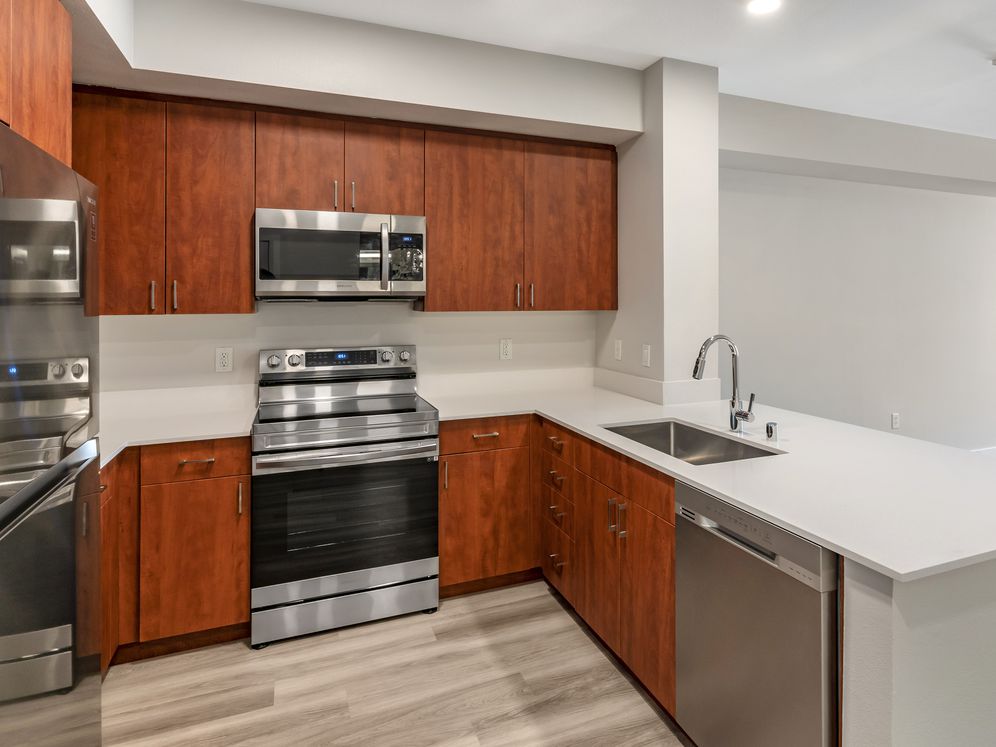 Renovated Package I kitchen with stainless steel appliances, white quartz countertops, cherry cabinetry, and hard surface flooring