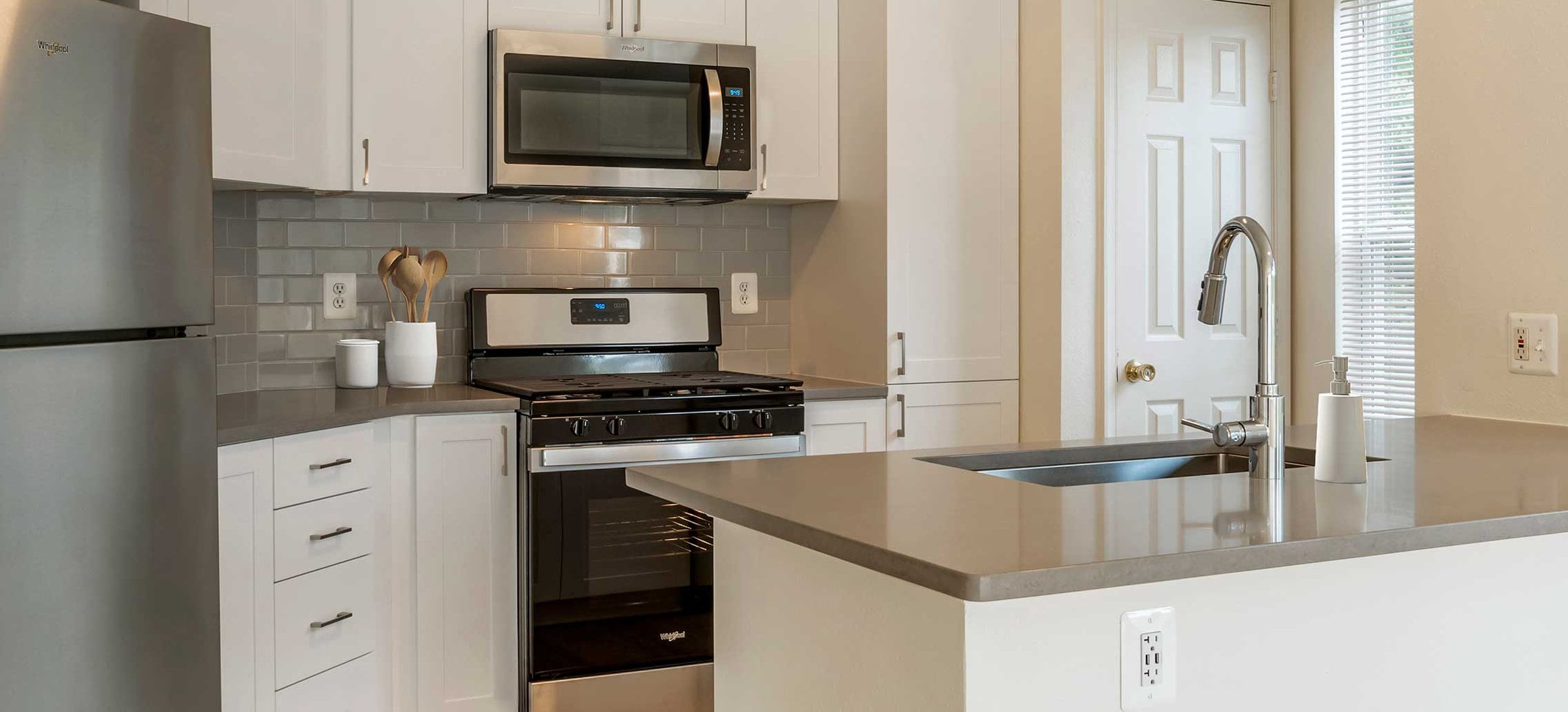 Newly renovated Finish Package V kitchens with white cabinetry, grey quartz countertops, stainless appliances, grey tile backsplash, and hard surface flooring