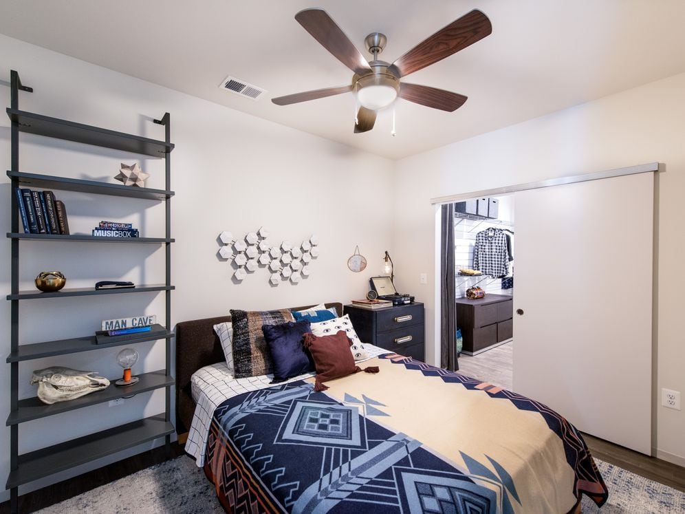 Bedroom with hard surface flooring, ceiling fan and barn door to customizable closet