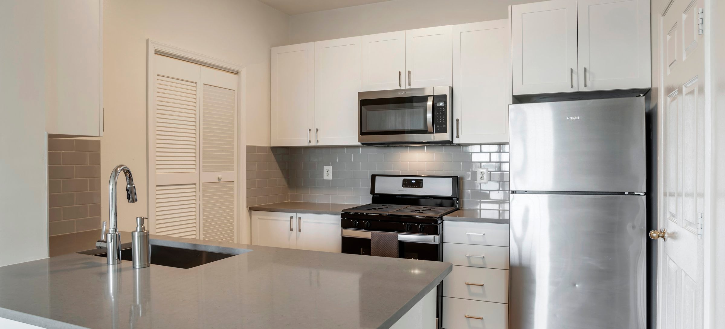 Renovated Package II kitchen with white cabinetry, grey quartz countertops, stainless steel appliances and tile backsplash