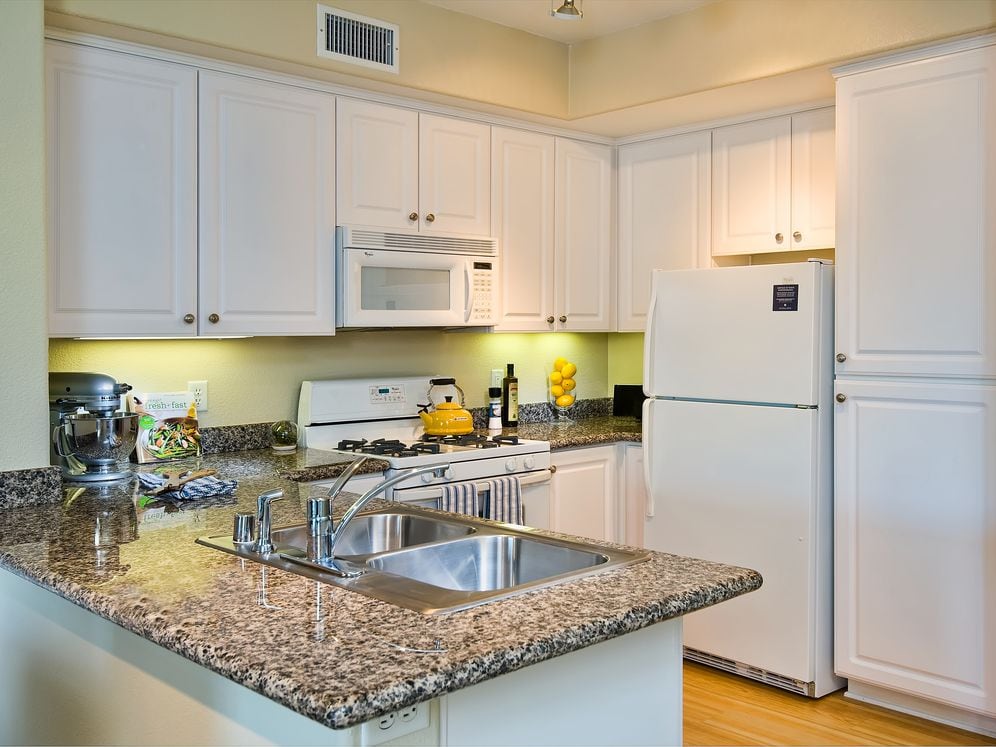 Classic Package I kitchen with white appliances, beige speckled granite countertop, white cabinetry, and hard surface flooring