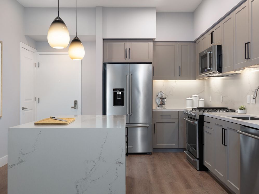Signature Collection kitchen with upgraded stainless steel appliances, grey cabinetry, white marble countertops and backsplash, and hard surface flooring 