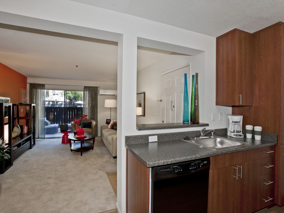 Kitchen with cherry cabinetry, living area with carpeted flooring