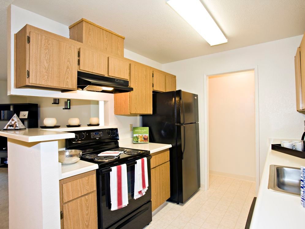 Kitchen with oak cabinetry, white countertops, black appliances and tile flooring